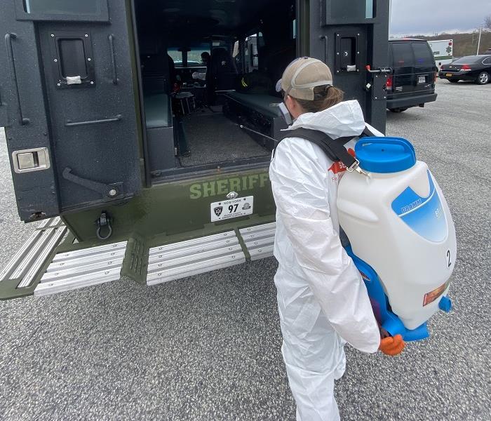 SERVPRO technician clad in PPE applying disinfectant to vehicle