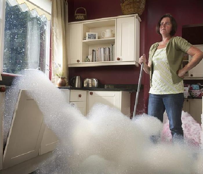 Frustrated woman watching suds leak from dishwasher