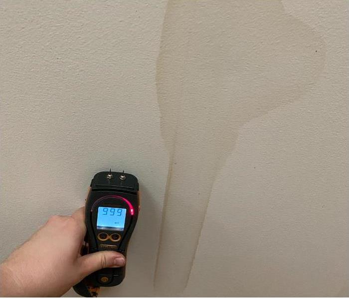 technician holding a moisture meter on a water damaged wall