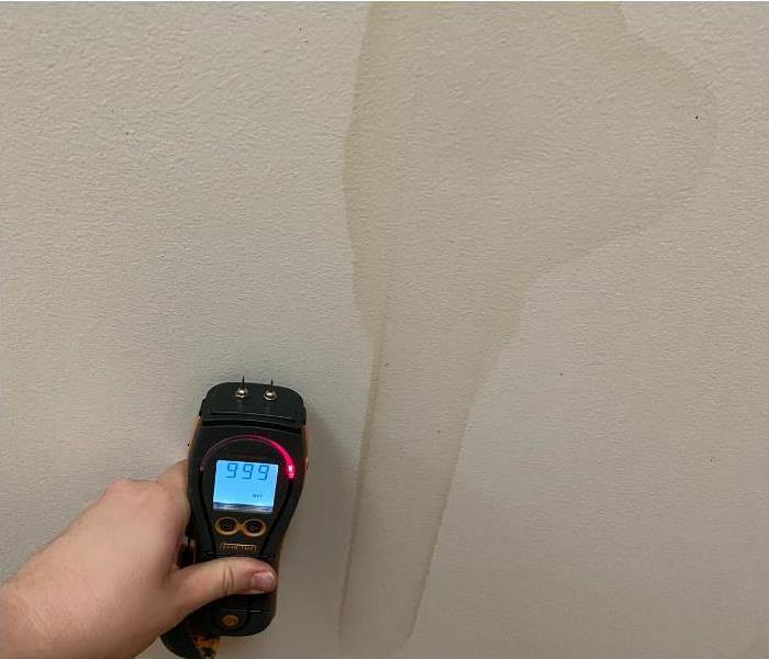 technician holding a moisture meter on a water damaged wall
